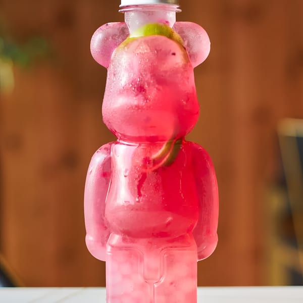 A pink, bear-shaped bottle of Romeo Tea, filled with a cold beverage and fruit slices.