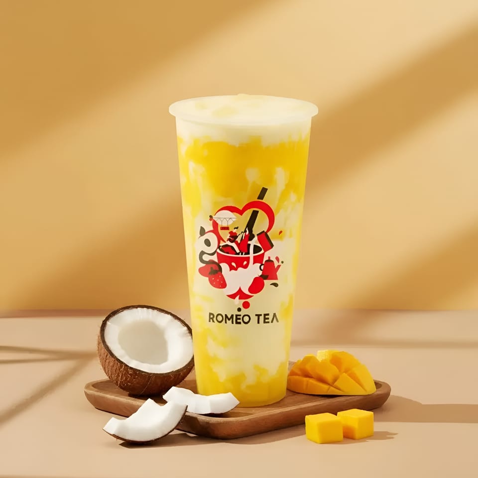 Romeo Tea mango and coconut drink with mango slices and coconut pieces on a wooden tray.